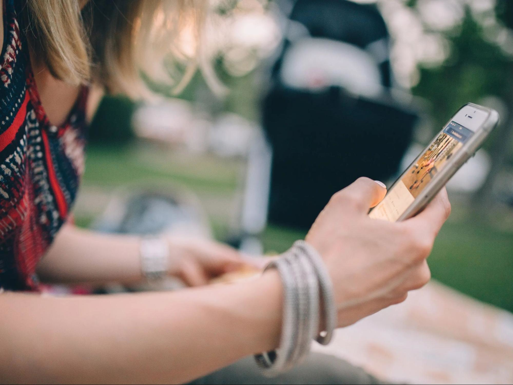 Someone sitting in a park in the sunshine checks their social media on their smartphone
